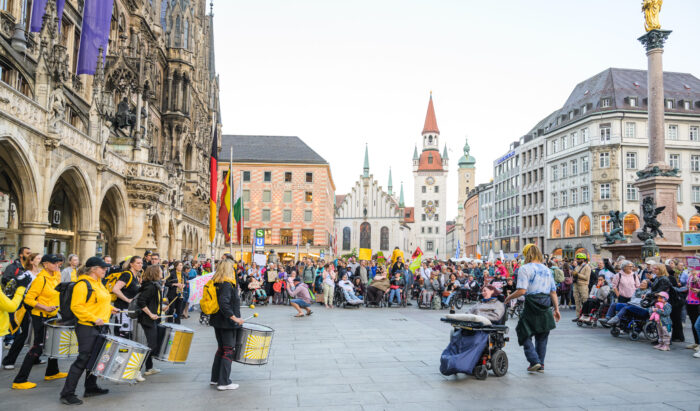 Die Demo auf dem Mariennplatz. In der Mitte eine Person in Rollstuhl, die mit einer anderen Person tanzt. 